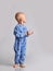 Barefooted baby boy in blue fleece jumpsuit with stars stands side to camera looking back at upper corner