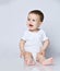 Barefooted baby boy toddler in white bodysuit is sitting on the floor looking sideways with opened mouth saying singing