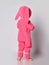 Barefooted baby girl in pink warm comfortable jumpsuit with hood on and bunny ears stands back to camera