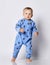 Barefooted blond baby boy in blue fleece jumpsuit with stars stands, going to run, peering out