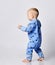 Barefooted blond baby boy toddler in blue fleece jumpsuit with stars stands walks holding hands up. Side view