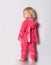 Barefooted blonde baby girl in pink warm jumpsuit with hood with bunny ears stands back to camera looking aside