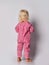 Barefooted blonde baby kid girl in pink warm comfortable jumpsuit stands back to camera over grey wall background