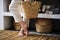 Barefooted female legs in short linen trousers on a straw mat against the background of baskets and shelves with towels