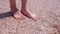 Barefooted girl traveller massaging feet on sandy beach in seashells at seaside.