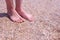 Barefooted girl traveller massaging feet on sandy beach in seashells at seaside.