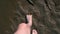 Barefooted man is walking on wet sand on riverbank, closeup feet.