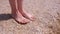 Barefooted woman massaging her feet on sandy beach in seashells on vacation.