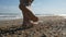 Barefooted woman tourist walks on sea shells on sand beach makes nature feet massage, side view. Girl traveller travel