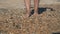 Barefooted woman tourist walks on sea shells on sand beach makes nature feet massage, side view. Girl traveller travel