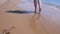 Barefooted woman tourist walks in water on sea sand beach, legs closeup.