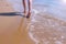 Barefooted woman tourist walks in water on sea sand beach, legs closeup.