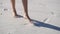 Barefooted woman walks on white sand in a sunny day