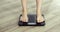 Barefooted woman weightning on digital modern scales at home, feet closeup.
