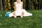 Barefooted young fair-haired bride sits on the grass in an exotic park