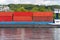 A barge carrying many containers on the Rhine in western Germany, trees and buildings in the background.