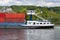 A barge carrying many containers on the Rhine in western Germany, trees and buildings in the background.