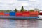 A barge carrying many containers on the Rhine in western Germany, trees and buildings in the background.