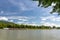 A barge flowing on the river Rhine in western Germany with a blue sky with clouds and a forest in the background.