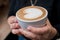 Barista girl holding fragrant freshly made cappuccino in her hands.