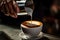 Barista pouring milk in a cup of coffee, close up. Barista pouring milk into a cup of latte art coffee. A coffee cup in a close up