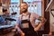 Barista with stylish beard and hairstyle wearing apron smiling and looking sideways while leaning on a counter in the