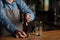 Barman in apron opens bottle of beer. Nearby empty glass on wooden bar counter