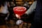 Barman holding a red alcoholic cocktail in a crystal glass with ice