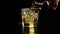 Barman pouring whiskey in the glass with ice cubes on wood table and black dark background, focus on ice cubes, whisky relax time