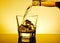 Barman pouring whiskey in the glass on table with reflection, warm tint atmosphere