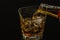 Barman pouring whiskey with ice cubes in glass on black background, cool atmosphere