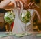 Barmans hand decorating two glasses of alcohol cocktail drinks arranged in a line. Bartender at work in bar.