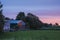 Barn on a farm light up by rising morning sun. Sunrise scene in a county side. Light pastel colors. Simple rural environment