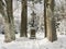 Baroque iron cross on sandstone pedestal with crucifix along snowy path with big beech trees at snow covered spruce tree