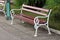 Baroque style shiny brown wood and white wrought-iron public bench mounted on stone tiles sidewalk with grass and small palm tree