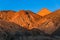 Barren desert mountains and a high peak glow in the golden hour of sunset under a perfect blue sky