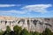 Barren erroded landscape in Badlands National Park with trees in foreground and a blue cloudy sky