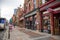 Bars and restaurants along Broadway with neon signs and red brick buildings with cars and trucks driving on the street and people