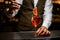 bartender accurate holding tweezers with citrus slice over wine glass with iced cocktail