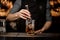 Bartender adding a big ice cube to the measuring glass cup with a brown cocktail