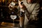 Bartender carefully pours drink from metal jigger into shaker on bar counter