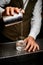 bartender carefully pours drink from steel mixing cup into old-fashioned glass