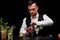 A bartender opens a shaker, a bar counter with margarita glasses, lemon, lime, cocktails on a black background.