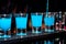 Bartender pours blue alcoholic drink into small glasses on bar