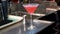 Bartender pours cocktail into a glass from shaker on counter, close-up of Cosmopolitan cocktail
