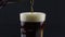 Bartender pours dark beer from a bottle into a glass. A man fills a glass with dark beer.