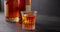 bartender puts ice cubes for cooling into a glass of whiskey on a background of bottles