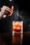 Bartender squeezes orange peel and sprinkles juice over the Negroni in the glass. Bartender prepares classical Negroni