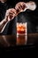 Bartender squeezes orange peel and sprinkles juice over the Negroni in the glass. Bartender prepares classical Negroni