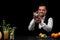 A bartender wipes a shaker at the bar counter, lemon, lime, oranges, cocktails on a black background.